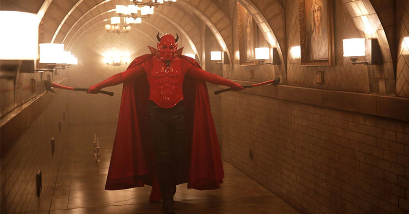 The Red Devil from Scream Queens walking down a hallway dragging axes along the walls