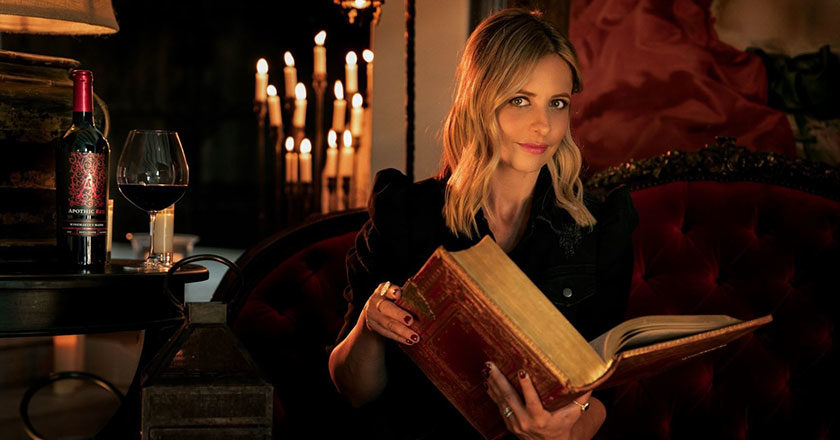 Sarah Michelle Gellar holding a large old book in a candlelit room.