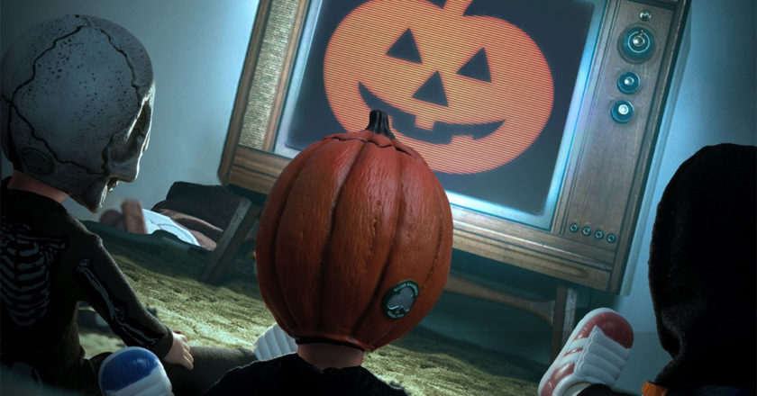 Halloween III trick-or-treaters dolls sitting in front of a TV with a jack-o-lantern on the screen