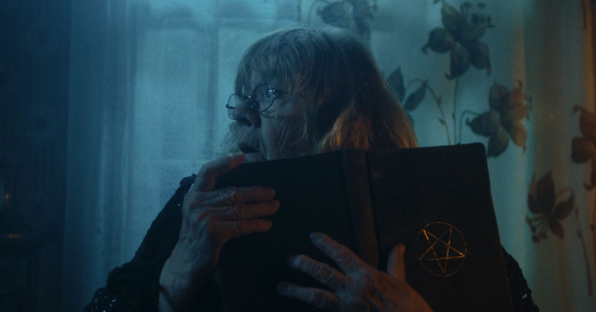 A still from "Kratt" featuring Grandma in a dark room holding a book with a pentacle on it